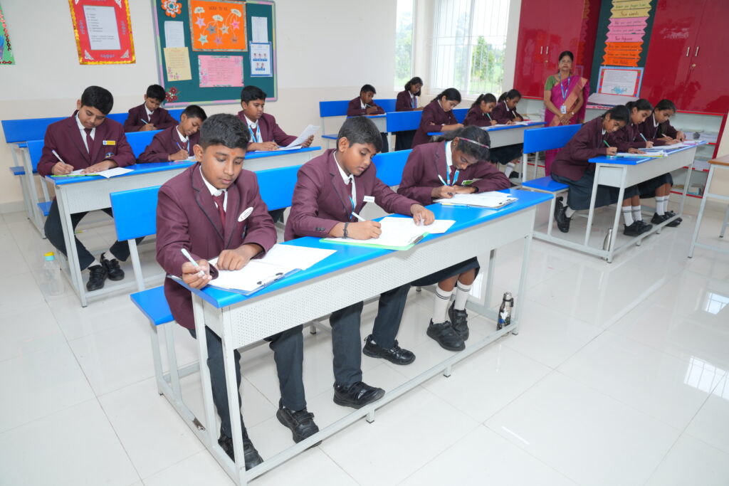Aadya Academy Budigere students in maroon blazers writing attentive in a well-lit modern classroom