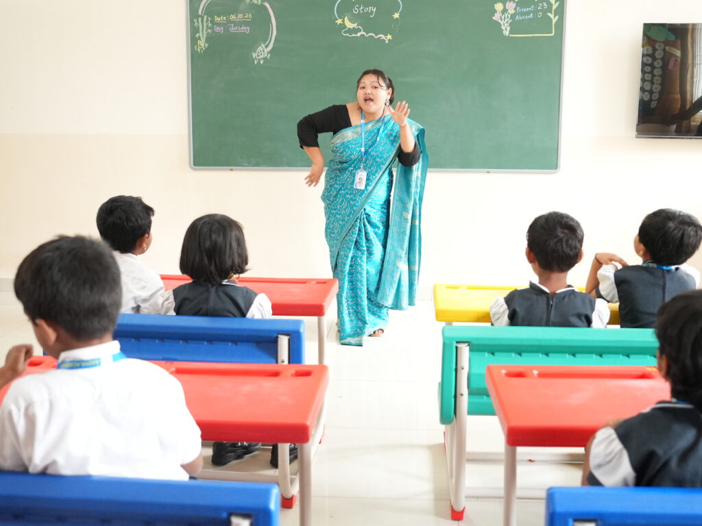 Aadya Academy Budigere primary teacher in saree conducting animated storytelling session for young students in a colorful classroom