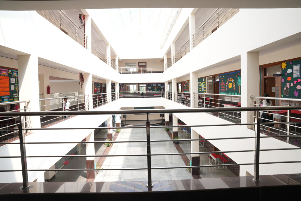 Multi-story indoor central atrium with skylight and stainless steel railings at Aadya Academy Budigere campus